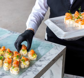 <img src=Γάντια νιτριλίου μαύρα χωρίς πούδρα alt=Σερβιτόρος με μαύρα γάντια τοποθετεί τα γλυκά στον δίσκο>